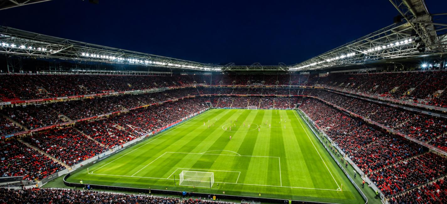 Aerial view of a packed English football stadium with red seats under floodlights on opening night